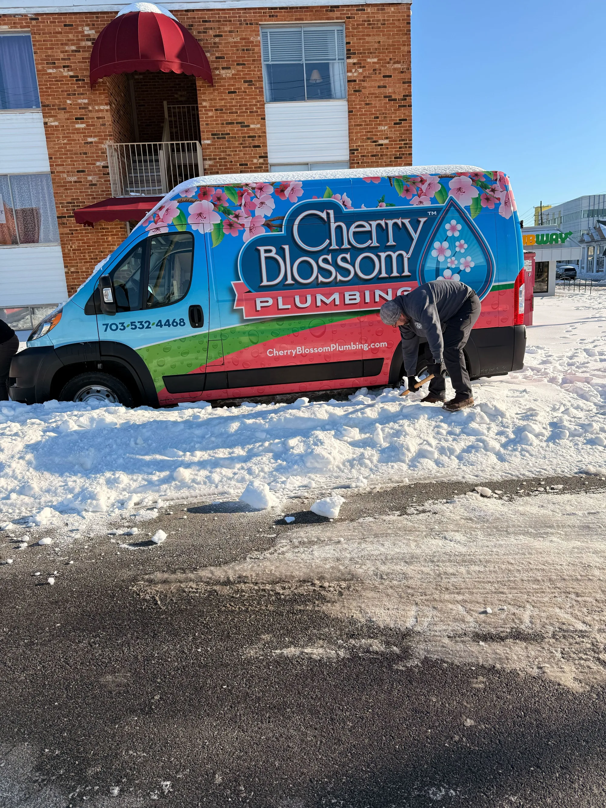Technician clearing snow around a Cherry Blossom Plumbing van