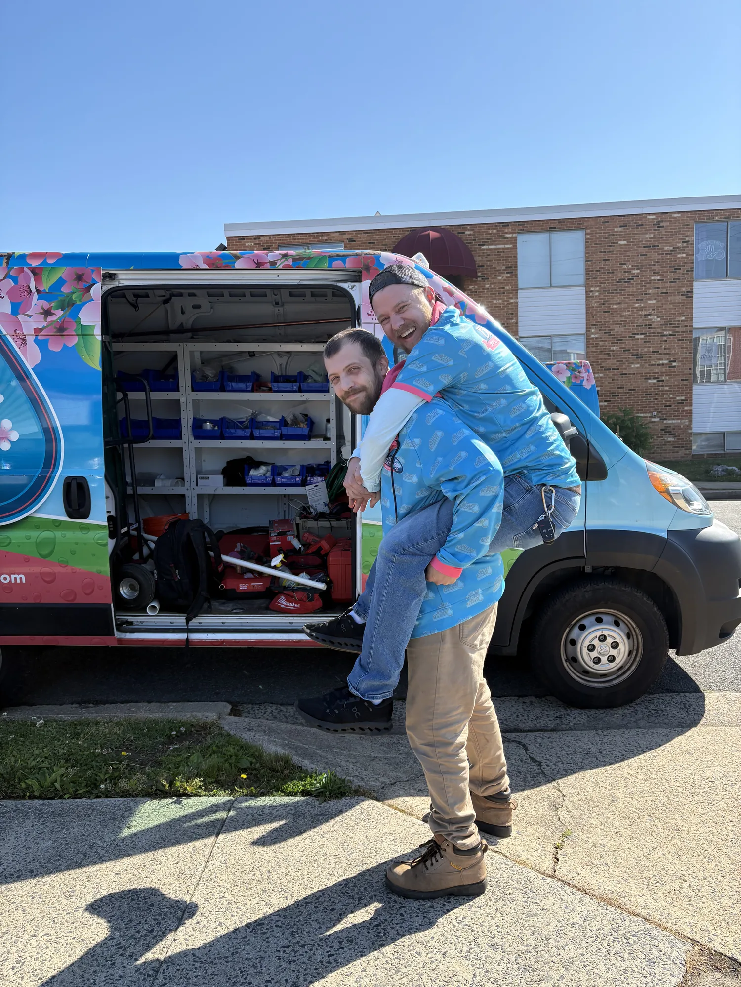 Two Cherry Blossom Plumbing technicians smiling at an open service van stocked with tools